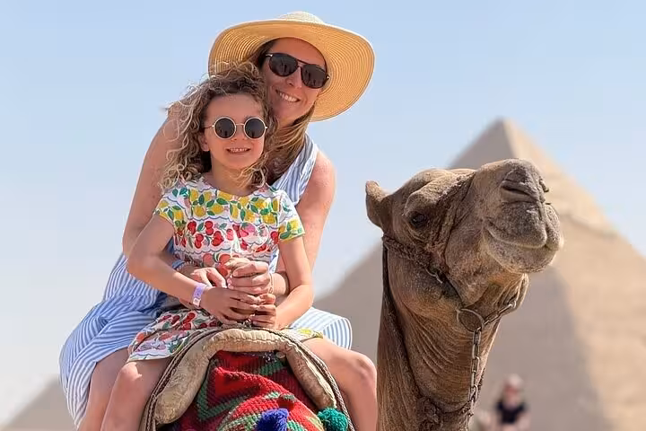 Mother and child on camel with Giza Pyramids behind, family tour led by expert female Egyptologist in Cairo