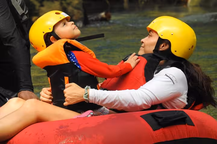 Mother and child bonding while tubing in Rio Celeste's clear waters, wearing safety gear.