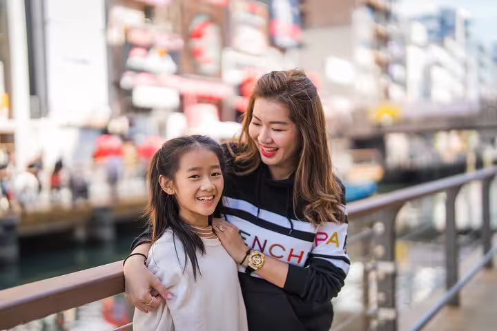 Mother and daughter smiling on a bridge in Osaka during a private photoshoot, capturing vibrant city life.