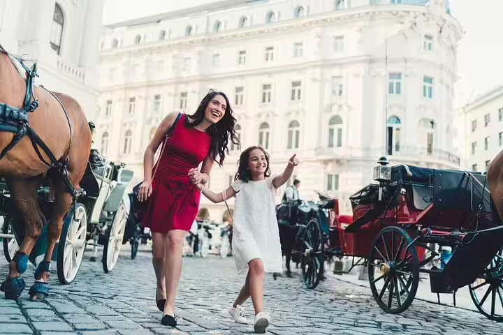 Mother and daughter joyfully explore Vienna's historic streets, surrounded by elegant architecture and horse-drawn carriages.