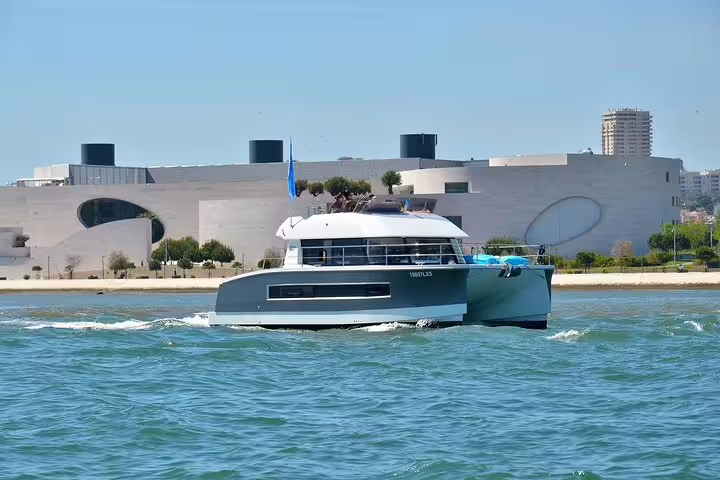 Modern motor catamaran cruising near Lisbon's waterfront, ideal for group tours up to 18 people.