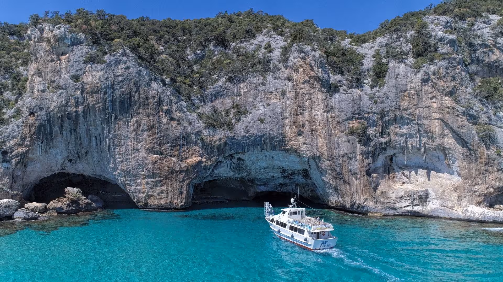 Motorboat approaching the entrance of Bue Marino Caves surrounded by dramatic cliffs and azure sea in Sardinia.