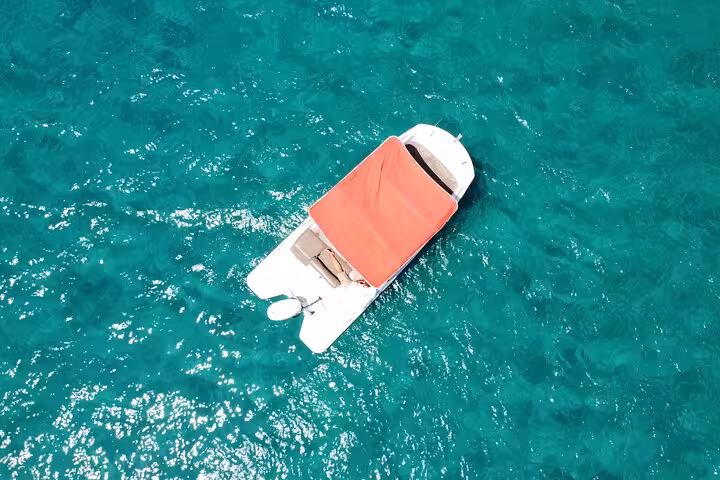 Aerial shot of a motorboat with a red canopy floating on Ibiza's sparkling blue sea, ideal for relaxed exploration.