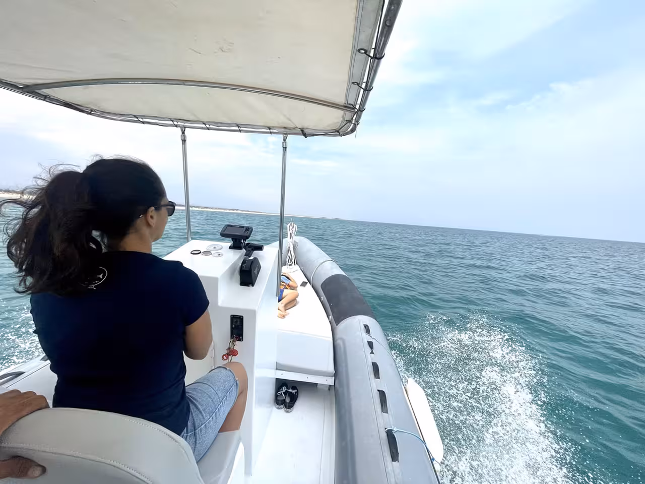 Woman steering a motorboat rental in Cabanas de Tavira cruising the calm Algarve sea with canopy shade