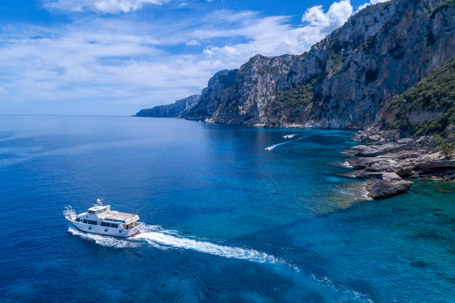 Motorboat cruising along stunning rocky coastline and azure sea near Cala Gonone en route to Bue Marino Caves.