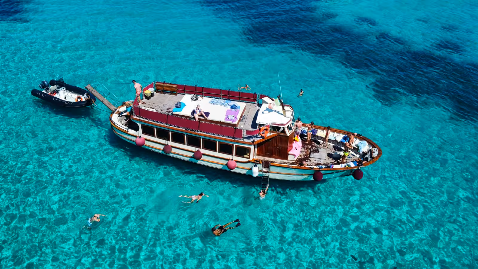 Tourists enjoying a sunny day on a motorboat in the clear waters of La Maddalena Archipelago, snorkeling nearby.