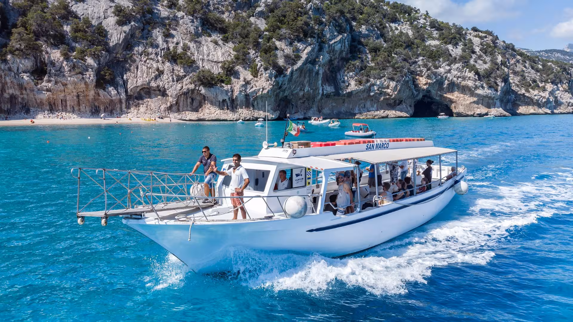 Tourists enjoying a motorboat ride in the Gulf of Orosei, showcasing stunning cliffs and clear blue waters.