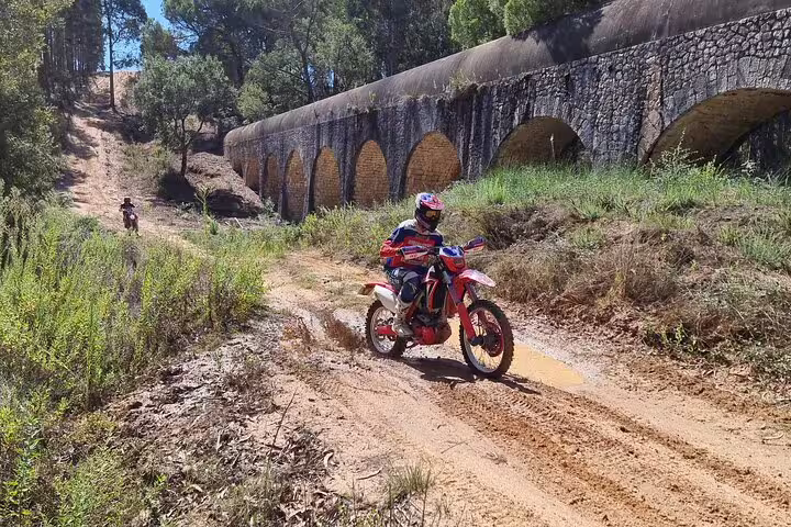 A motorcyclist navigates a sandy trail beside a historic aqueduct during a Lisbon enduro adventure.