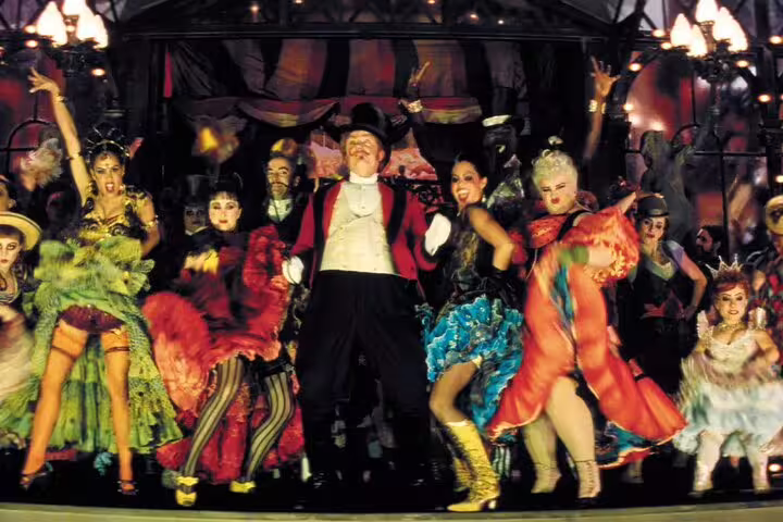 Moulin Rouge performers dancing on stage in colorful costumes with ringmaster in Paris cabaret show