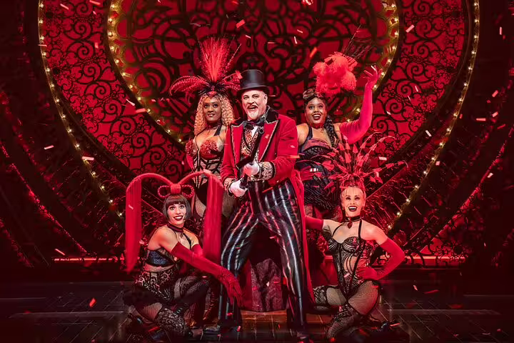 Moulin Rouge performer in red tailcoat with showgirls on stage in Paris cabaret show