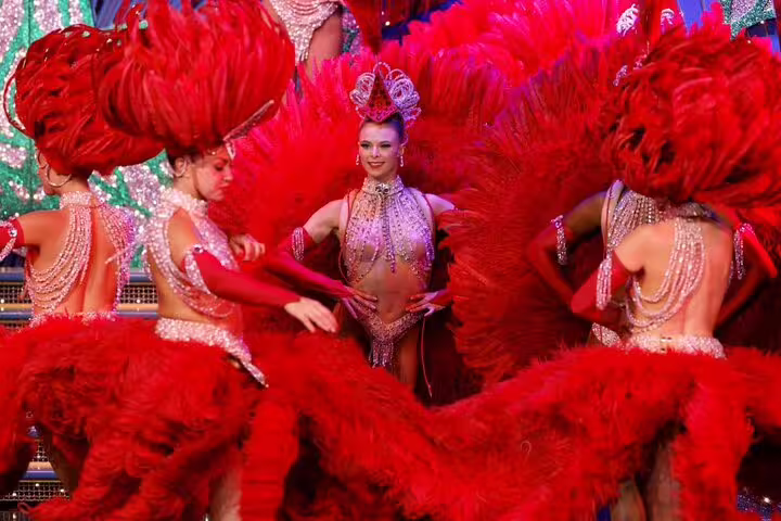 Moulin Rouge dancers in red feather costumes and jeweled bodysuits performing on stage in Paris