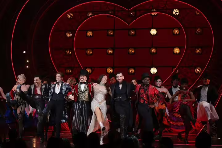 Moulin Rouge musical cast performing on stage with illuminated red heart backdrop