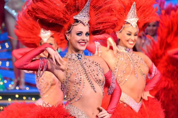 Moulin Rouge showgirls in red feathered costumes and rhinestone bodysuits performing on stage in Paris