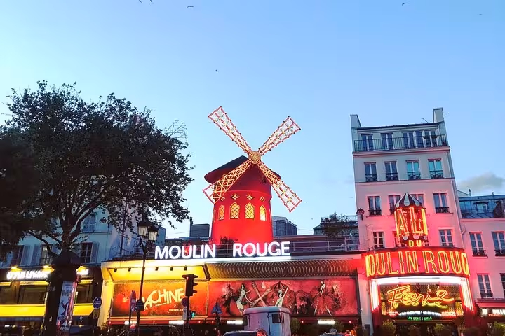 Moulin Rouge windmill lit up with red neon signs at dusk in Montmartre, Paris