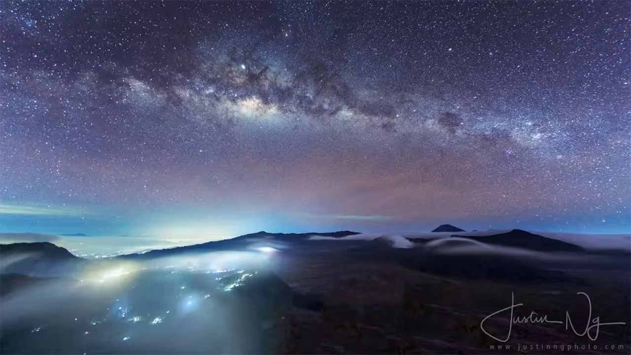 Stunning Milky Way view over Mount Bromo with glowing lights creating a magical nightscape, ideal for stargazing tours.