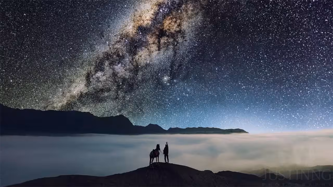 Silhouette of traveler with horse under a brilliant Milky Way sky at Mount Bromo, an unforgettable stargazing experience.