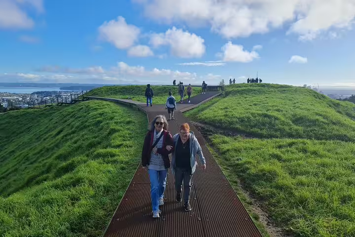 Visitors enjoying a sunny day atop Mount Eden, overlooking Auckland's stunning cityscape and harbor.
