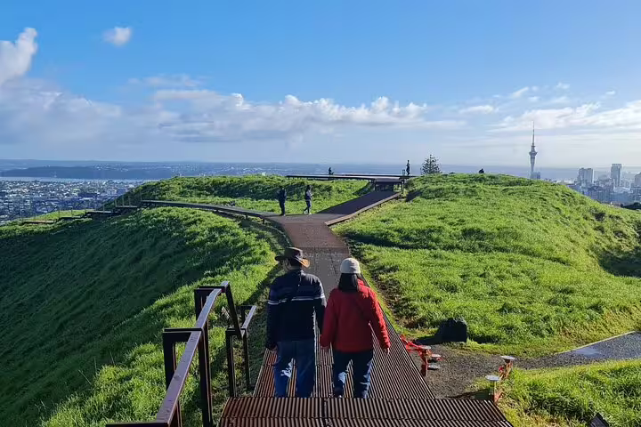Tourists walking along the lush green path on Mount Eden, offering panoramic views of Auckland City.