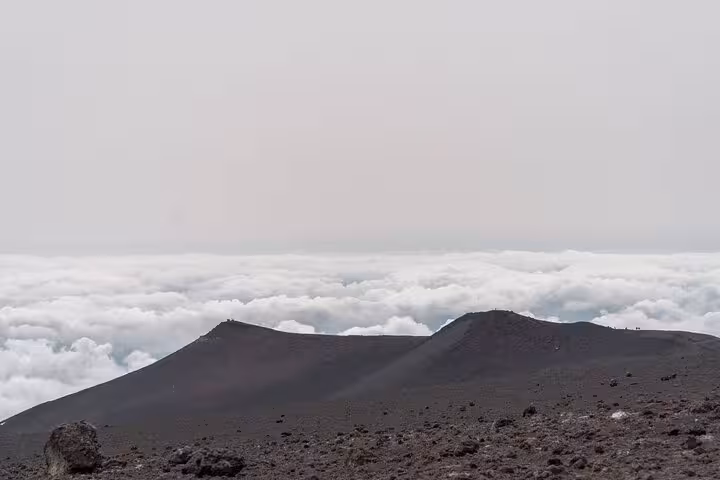 View from Mount Etna's summit, showcasing a dramatic volcanic terrain above the clouds on a guided tour.