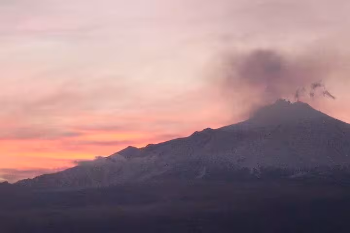 Breathtaking view of Mount Etna at sunset with vibrant pink and orange sky and smoke rising from the crater.