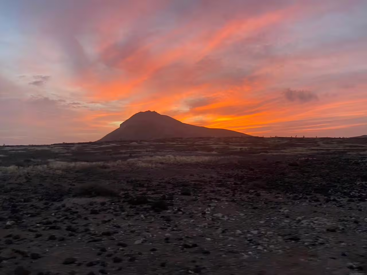 Mount Lion silhouette at golden hour with vivid clouds above volcanic plains on the Sunset Hiking to Mount Lion trek