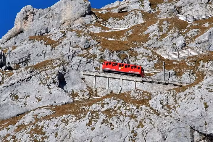 Red cogwheel train ascending the rocky slopes of Mount Pilatus, showcasing stunning alpine scenery.