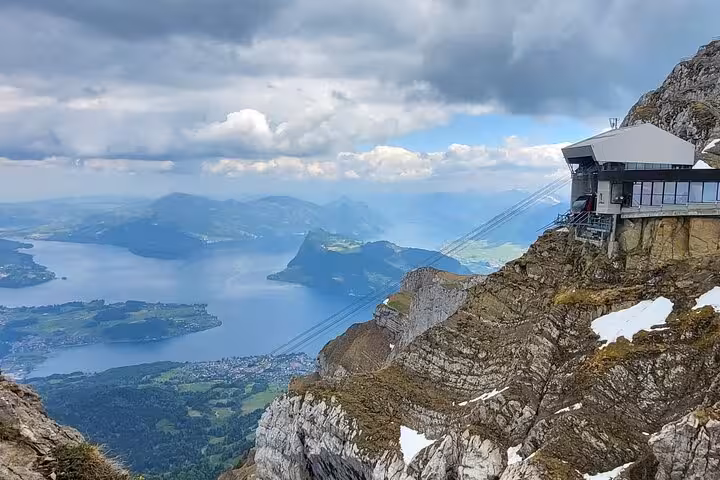 Breathtaking view of Lake Lucerne and Swiss Alps from Mount Pilatus, featuring a modern cable car station perched on rugged cliffs.
