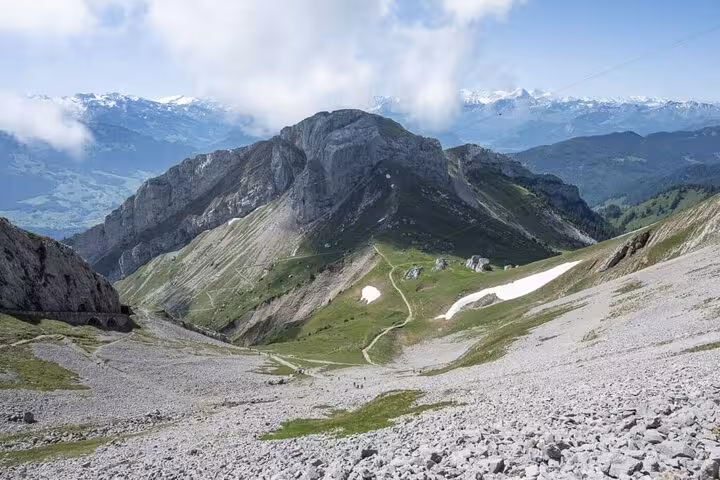 Majestic rocky landscape of Mount Pilatus with snow patches and stunning views of the Swiss Alps in the background.