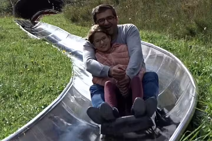 Father and daughter enjoying a thrilling summer toboggan ride in the lush green landscapes near Mount Pilatus.