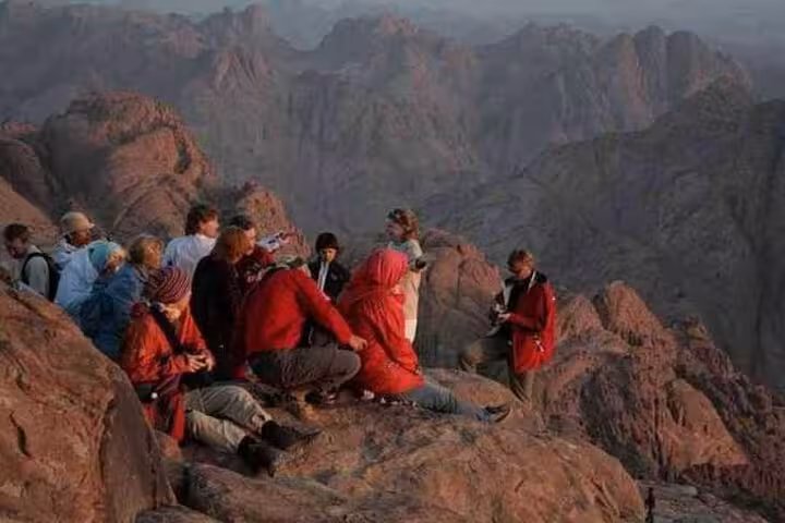 Travelers watching sunrise from Mount Sinai summit, guided hike from Sharm El Sheikh to Jebel Musa