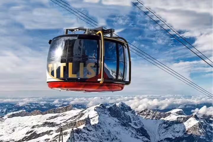 A rotating cable car ascends Mount Titlis, showcasing stunning snow-covered peaks and a clear blue sky.