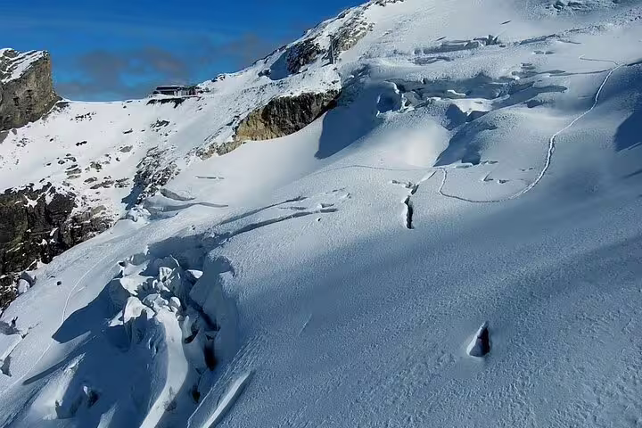 Snow-covered Mount Titlis glacier slopes with rocky cliffs and mountain station under blue sky