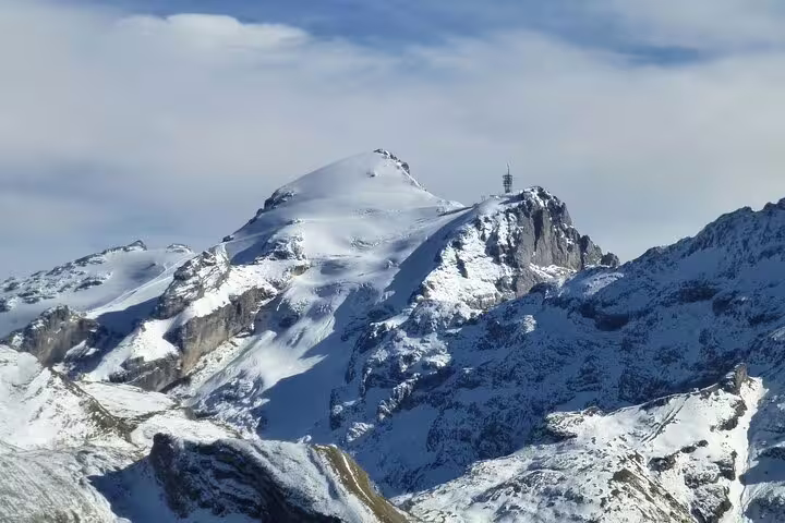 Snow-covered Mount Titlis summit with observation tower and rocky alpine terrain under blue sky