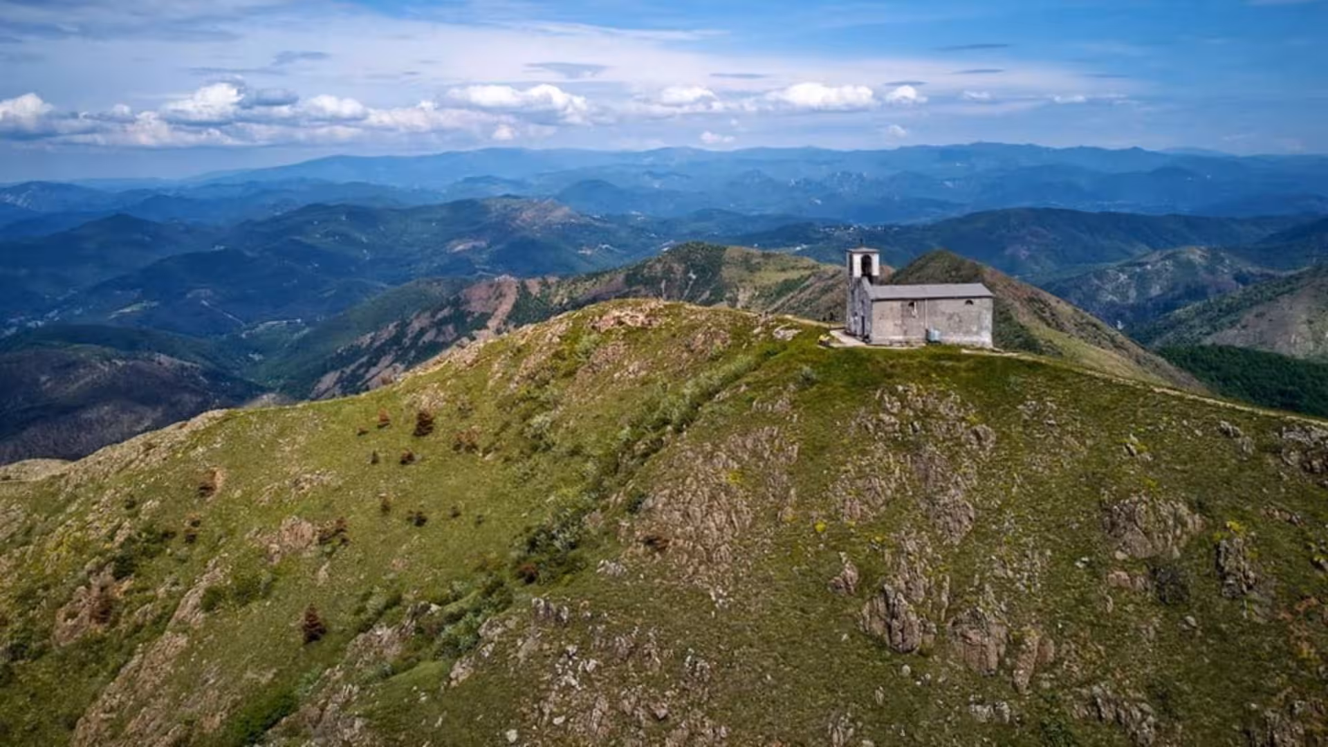 Aerial view of Mount Tobbio with a solitary church, showcasing expansive green landscapes and mountain vistas.