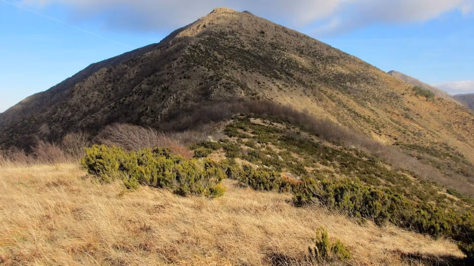 Breathtaking landscape of Mount Tobbio's rugged terrain, with dry grass and sparse vegetation under a clear sky.