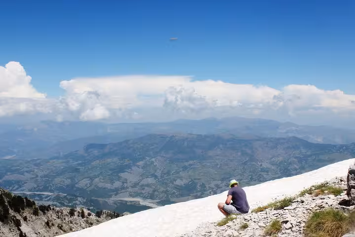 Traveler enjoying a panoramic view from Mount Tomorr's snowy peak, ideal for adventure enthusiasts seeking guided tours.