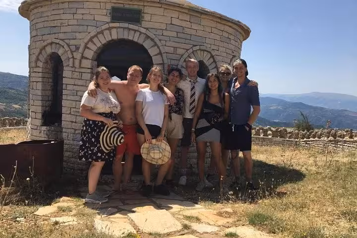 Group of hikers pose by a stone building atop Mount Tomorr, showcasing summer exploration in Albania.