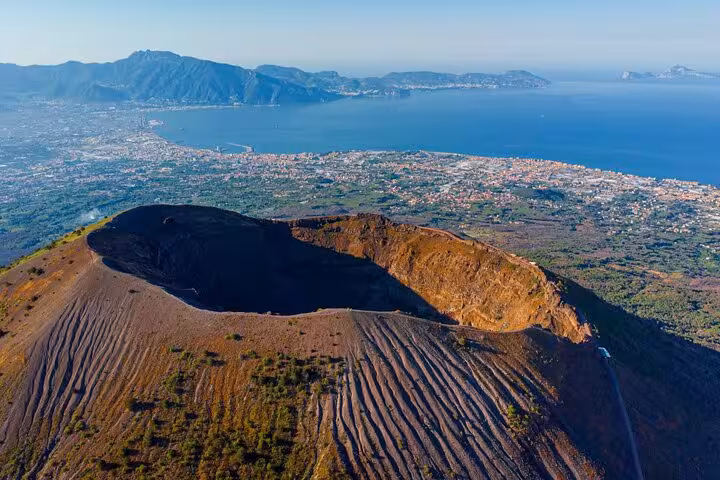 Aerial view of Mount Vesuvius crater with the scenic Bay of Naples in the distance, highlighting volcanic landscape.