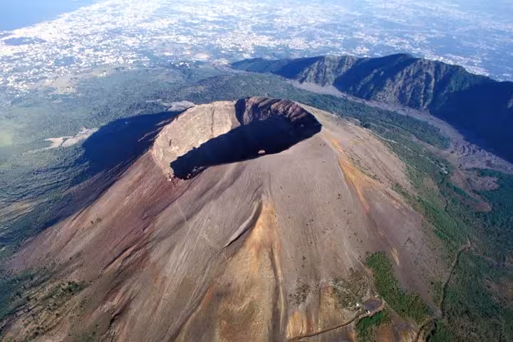 Aerial view of Mount Vesuvius crater surrounded by lush landscape, highlighting the adventure and wine tasting tour.