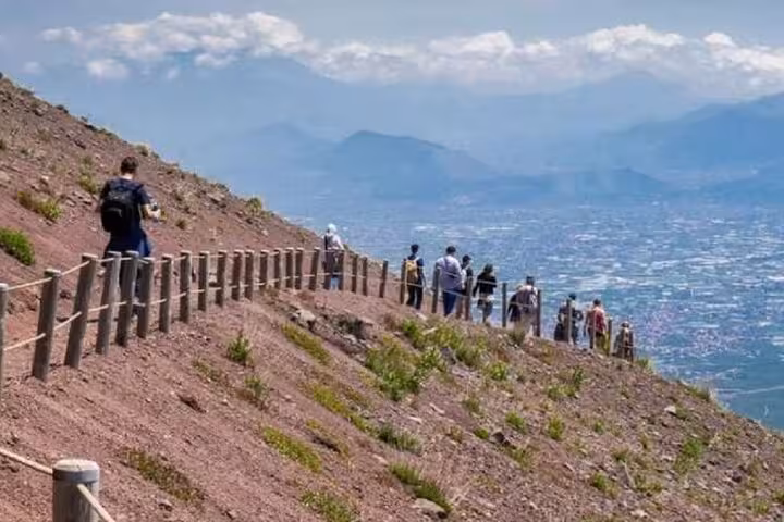 Tourists enjoy panoramic views of Naples while hiking the scenic trails of Mount Vesuvius on a sunny day.