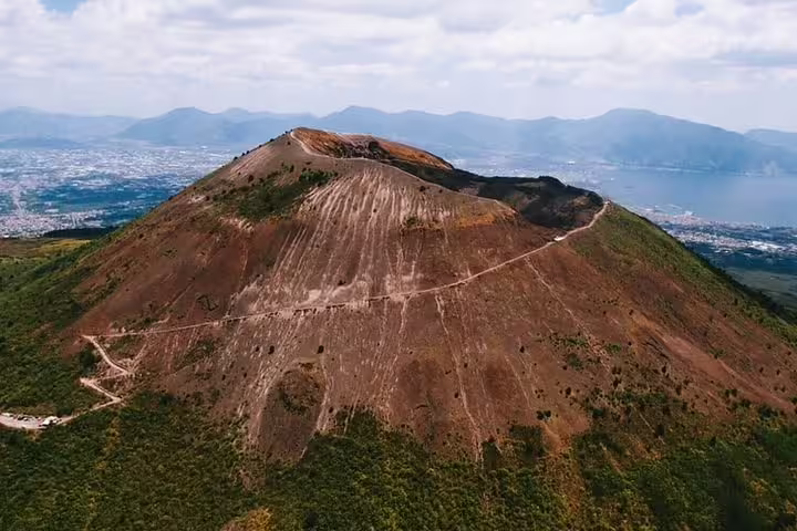 Panoramic drone shot of Mount Vesuvius hiking trail above Ercolano with Naples coastline on shore excursion day trip