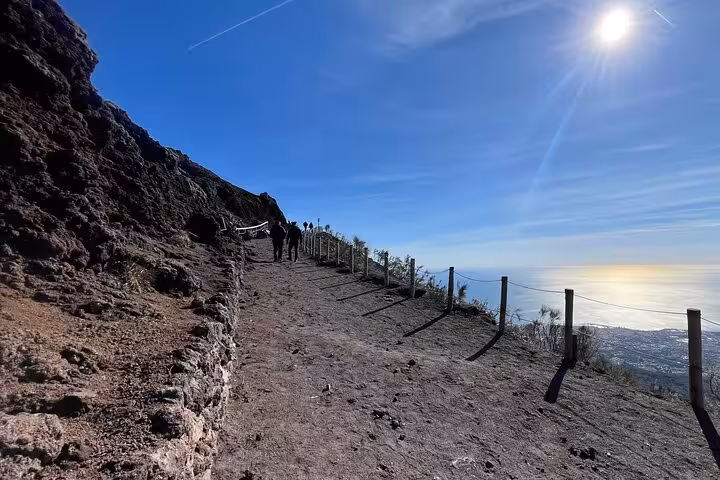 Hiking trail on the slopes of Mount Vesuvius with a stunning view of the sea and a bright sun overhead.