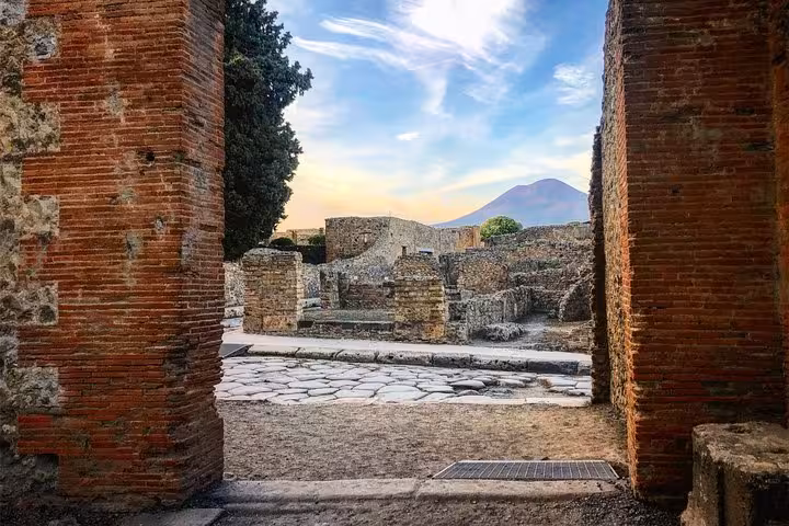View of Mount Vesuvius and ancient ruins through a stone archway in Pompeii on a guided tour from Sorrento Coast.