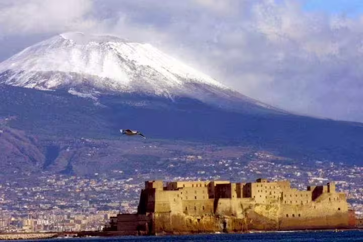 Snow-capped Mount Vesuvius rises above the Bay of Naples and Castel dell’Ovo, featured on a private Pompeii and winery tour