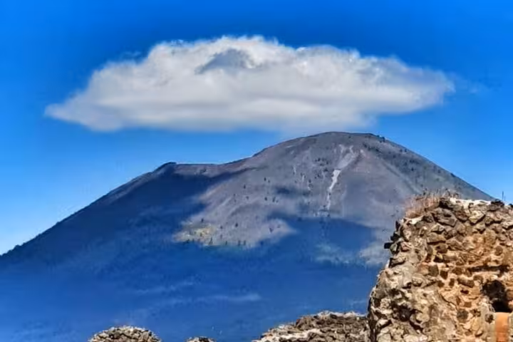 Majestic view of Mount Vesuvius under a cloud-dotted sky, ideal for a memorable tour with entry ticket and lunch.