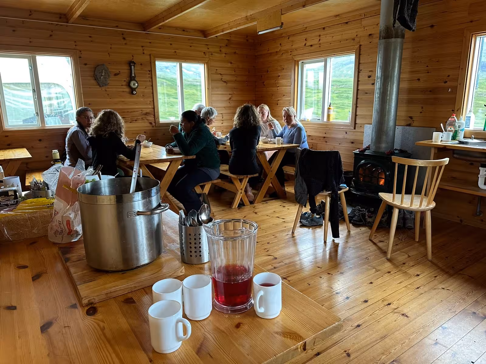 Hiking group enjoying a warm meal inside a cozy wooden mountain hut during a 5-day guided tour in East Iceland