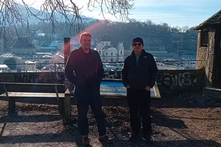Two men standing at a scenic Salzburg Old Town viewpoint with historic church and rooftops in background