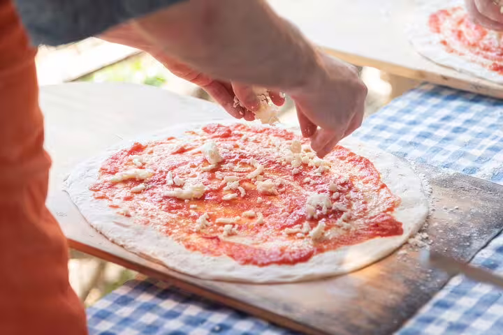 Adding mozzarella to tomato-topped pizza base in a local farm pizza class with wine and limoncello tasting