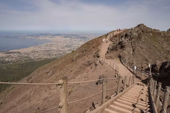 Tourists exploring the rugged trails of Mt. Vesuvius with stunning views of Naples on a volcano adventure.