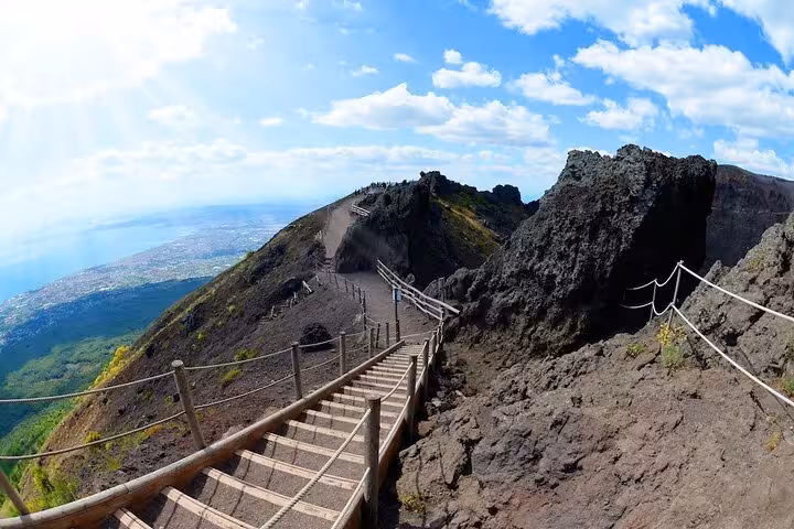 Wooden steps leading up Mt. Vesuvius with breathtaking views of rugged terrain and blue skies on a sunny day.